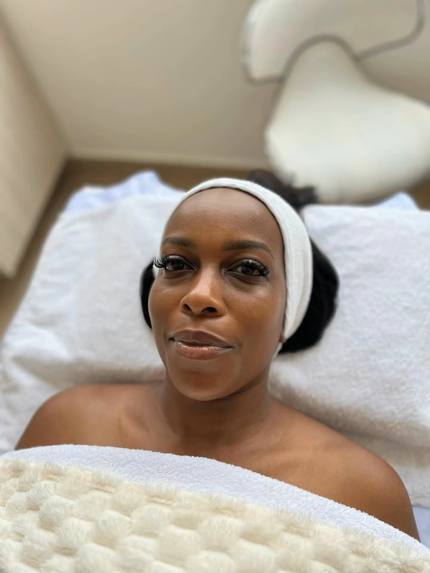 A client relaxing on the treatment bed at Skin by Lyze, wrapped in a warm towel before her esthetic facial